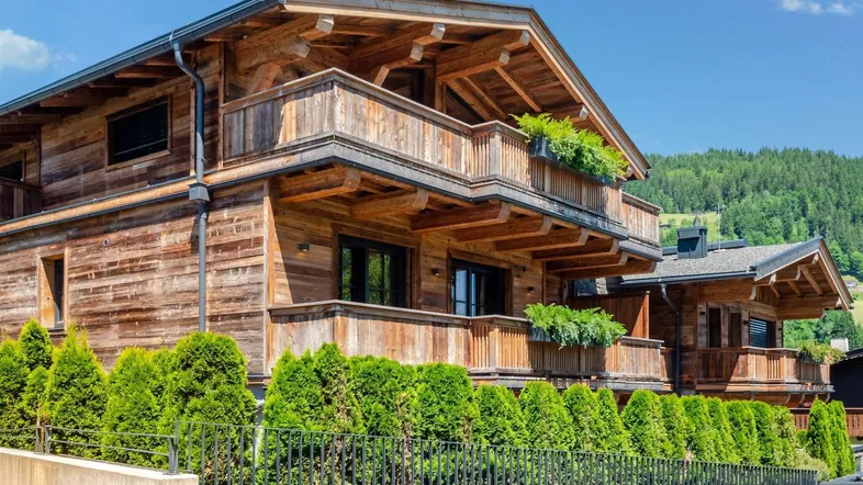 Charmantes Holzchalet mit mehreren Balkonen und gepflegten Hecken vor einer Bergkulisse.