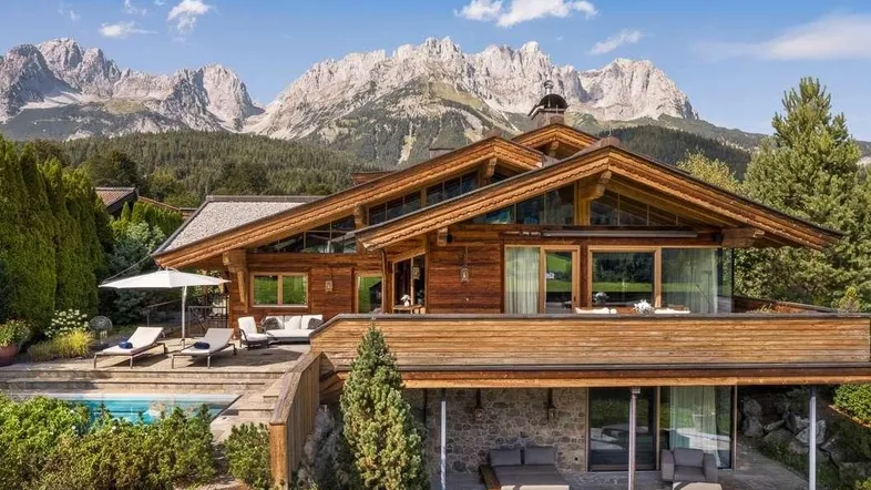 Luxuriöses Holzchalet mit privatem Pool und atemberaubendem Bergblick unter blauem Himmel.