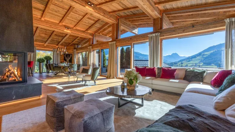 Großzügiger Wohn- und Essbereich im Chalet-Stil mit Kamin, Holzbalkendecke und Panoramablick auf die Berge.