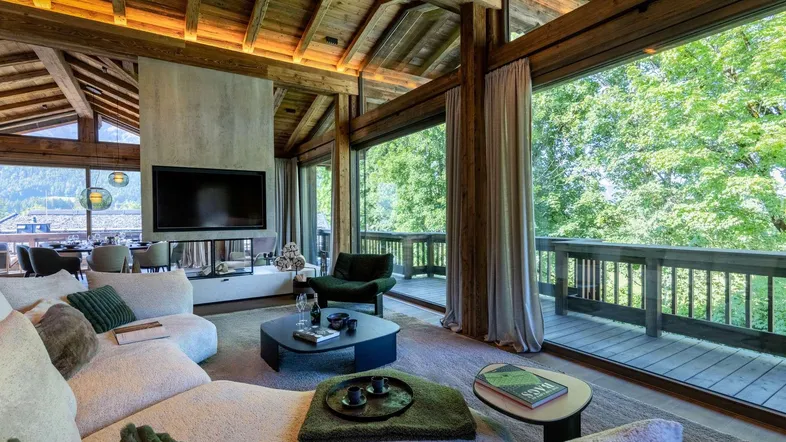 Geräumiges Wohnzimmer im Chalet-Stil mit Kamin, großen Fenstern und Bergblick.
