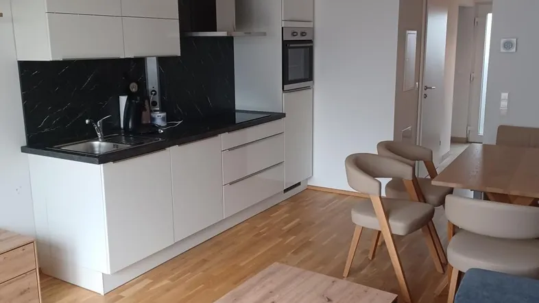 Moderne offene Küche mit weißen Schränken, dunkler Arbeitsplatte und angrenzendem Essbereich.