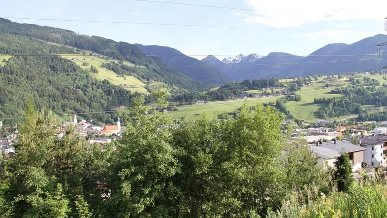 Weitläufiger Blick über ein grünes Tal mit Bergen und einer kleinen Stadt im Hintergrund.