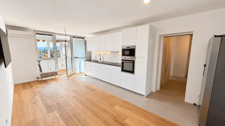 Helle, offene Wohnküche mit modernen weißen Schränken, Holzboden und Zugang zum Balkon.