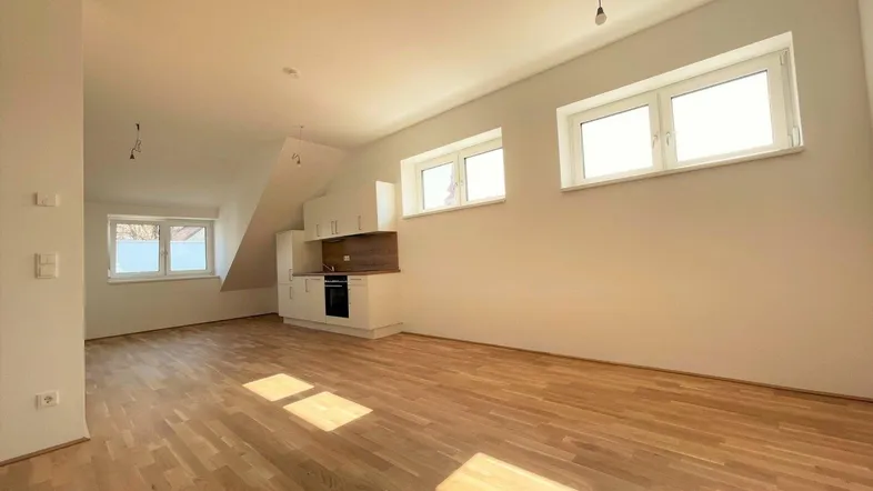 Helles, offenes Wohnzimmer mit Holzboden und integrierter Küchenzeile unter Dachschrägen.