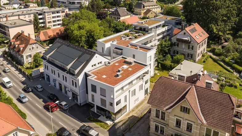 Luftaufnahme eines Wohnkomplexes mit umliegender Bebauung, Straße und Grünflächen.