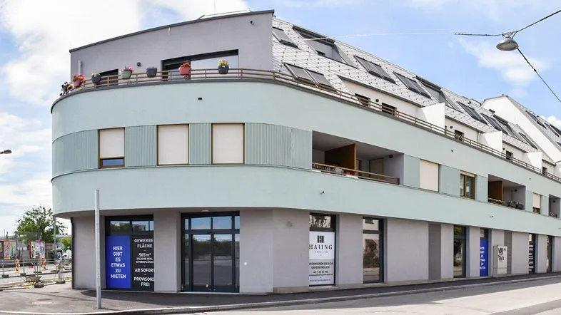 Modernes Gebäude mit abgerundeter Fassade und Geschäften im Erdgeschoss an einer Straßenecke.