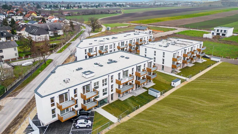 Luftaufnahme von modernen Wohngebäuden mit Flachdächern und Balkonen in ländlicher Umgebung.