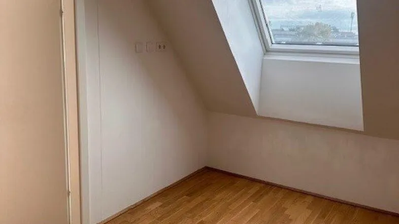 Helles Zimmer im Dachgeschoss mit Holzboden und großem Dachfenster, ideal als Schlafzimmer oder Büro.