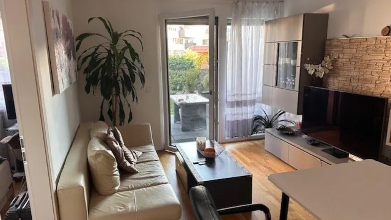 Helles Wohnzimmer mit Holzboden, beigem Sofa und Zugang zu einer Terrasse.