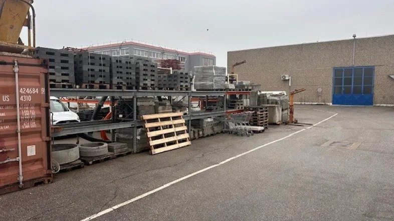 Industrieller Außenbereich mit gelagerten Baumaterialien und einem Gebäude im Hintergrund.
