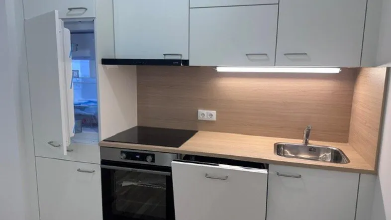 Moderne Einbauküche mit weißen Schränken, Holzoptik-Arbeitsplatte und integrierten Geräten.