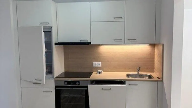 Moderne Einbauküche mit weißen Schränken, integrierten Geräten und hellem Holzfußboden.