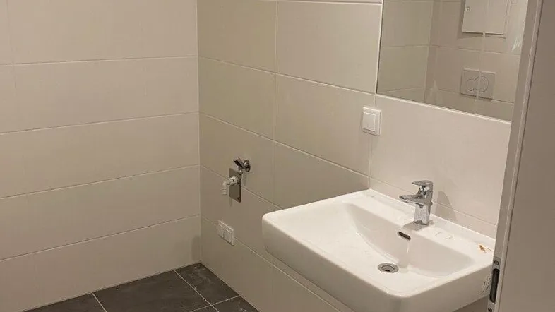 Modernes Badezimmer mit weißem Waschbecken, Spiegel und hellen Fliesen an Wänden und Boden.