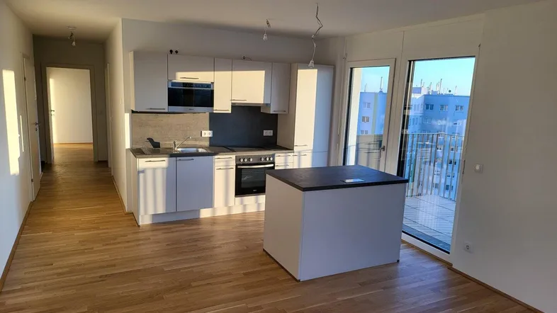 Helle offene Küche mit moderner Einbauküche, Kücheninsel und Zugang zum Balkon.