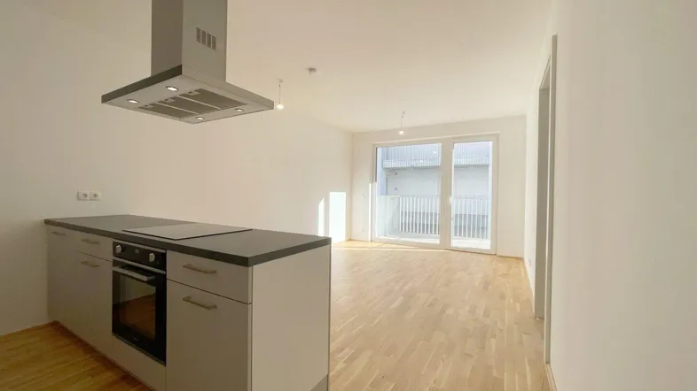 Heller, offener Wohn-Essbereich mit moderner Küchenzeile und Zugang zum Balkon.