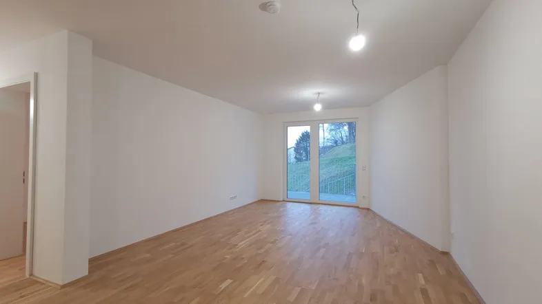 Helles, leeres Wohnzimmer mit Parkettboden und Zugang zu einem Balkon, bereit zum Einzug.