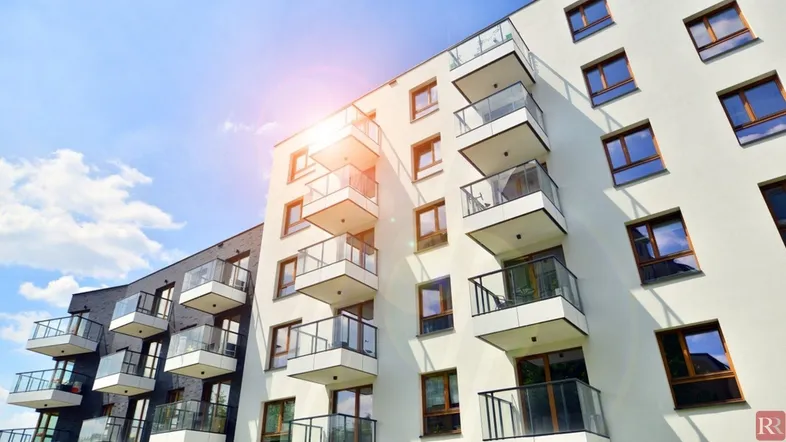 Moderne Wohngebäude-Fassade mit vielen Balkonen und großen Fenstern unter blauem Himmel.