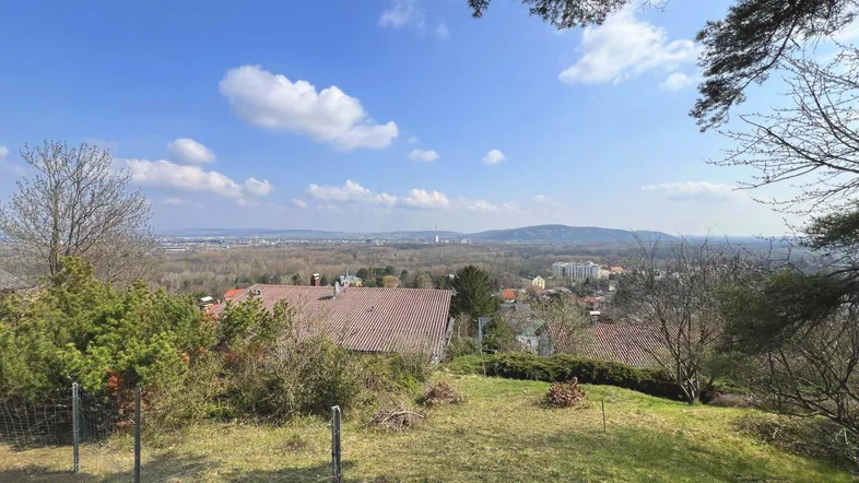 Weitläufiger Blick über die Landschaft mit Häusern und Bergen am Horizont unter blauem Himmel.