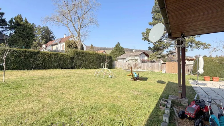 Gartenbereich mit hoher Hecke, Bäumen und Kinderspielgeräten.