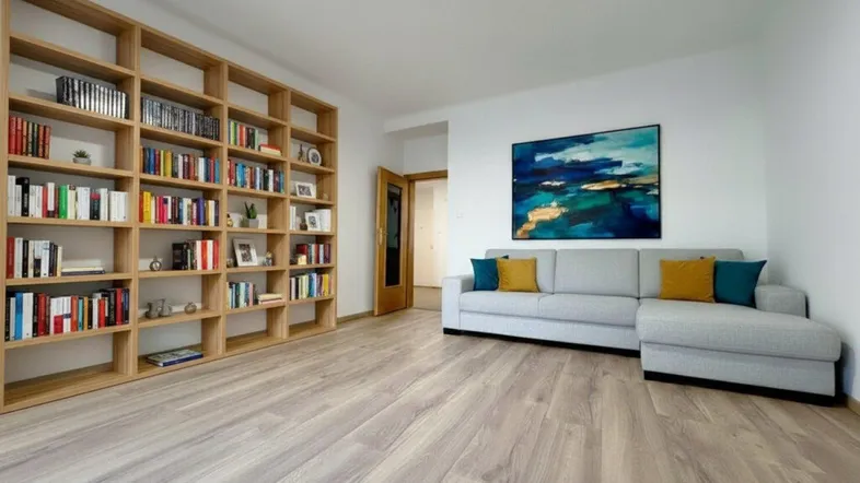 Helles Wohnzimmer mit großem Bücherregal, modernem Sofa und Holzboden.