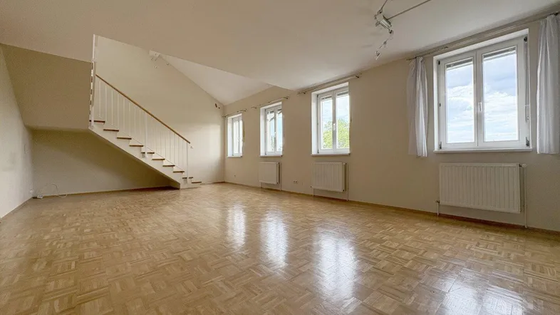 Geräumiger Wohnbereich mit hellem Parkettboden, vielen Fenstern und einer eleganten Treppe zum Obergeschoss.