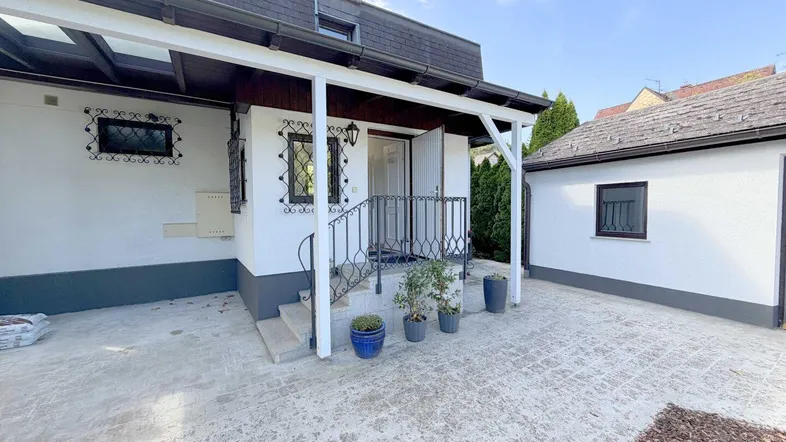 Überdachter Eingangsbereich des Hauses mit gepflastertem Vorplatz und Carport.
