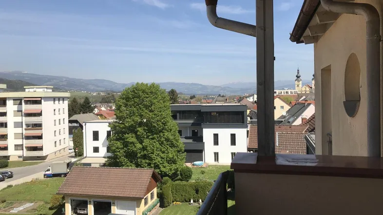 Blick vom Balkon auf die umliegende Landschaft mit Bergen und Häusern unter blauem Himmel.