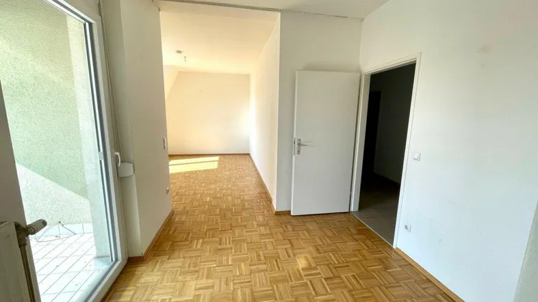 Helles Zimmer mit Parkettboden und Zugang zu einem Balkon, ideal als Wohnbereich nutzbar.