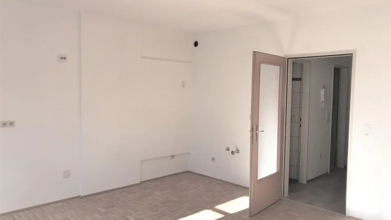 Helles, leeres Zimmer mit Parkettboden und weiß gestrichenen Wänden, bereit zur Einrichtung.