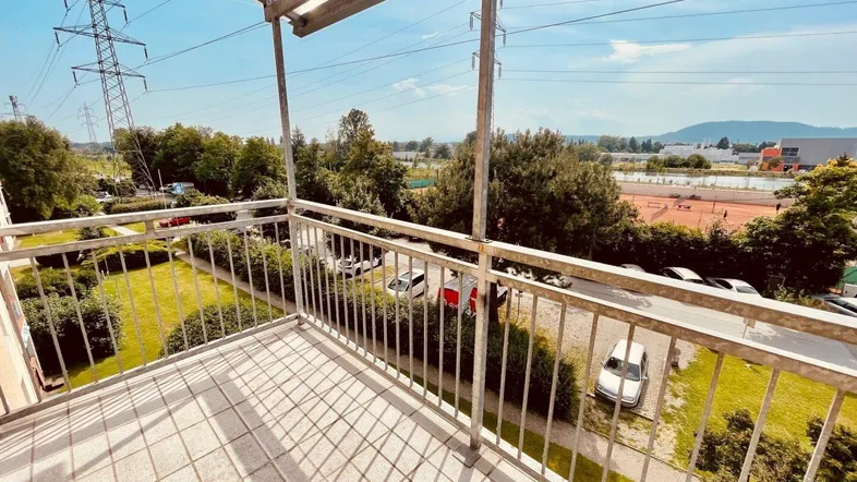 Geräumiger Balkon mit Metallgeländer, Überdachung und Blick ins Grüne sowie auf die Umgebung.