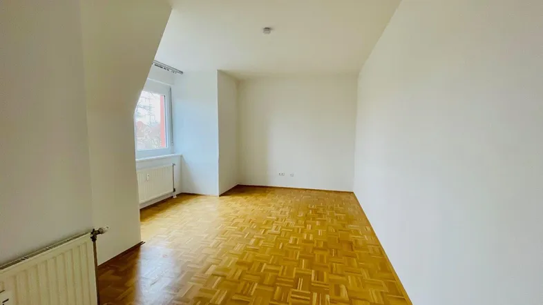 Helles, leeres Zimmer mit Parkettboden und Dachschräge, ideal als Wohn- oder Schlafzimmer.