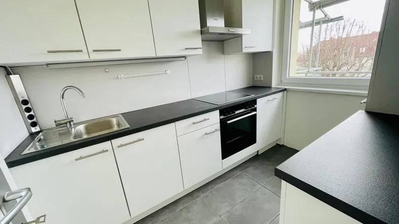 Moderne Einbauküche mit weißen Schränken, dunkler Arbeitsplatte und Fensterblick.