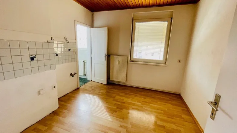 Leere Küche mit Holzdecke, Laminatboden und Fliesen an der Wand, bereit für eine neue Einrichtung.