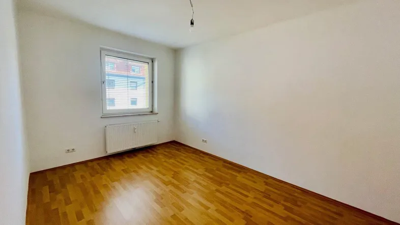 Helles, leeres Zimmer mit Laminatboden, weiß gestrichenen Wänden und einem Fenster.