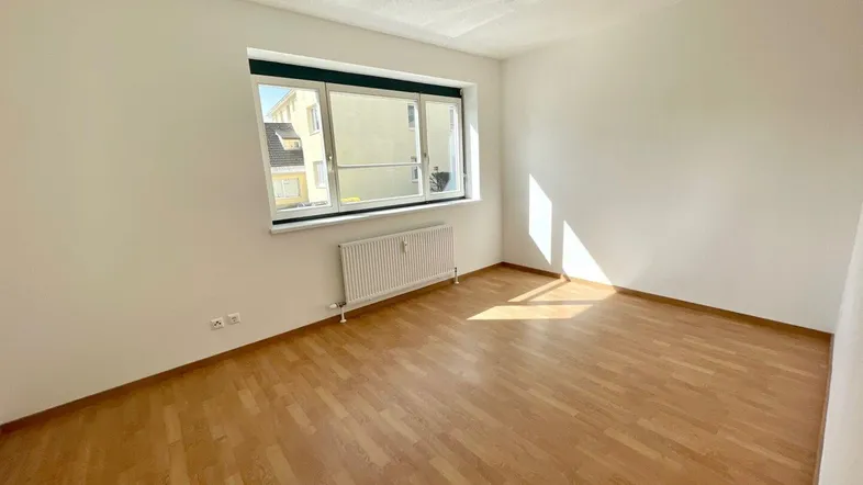 Helles Zimmer mit Laminatboden und Fenster, das viel Tageslicht hereinlässt.