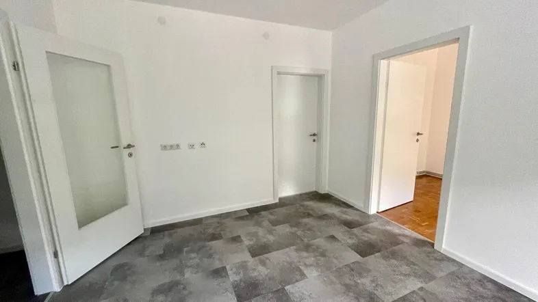 Leeres Zimmer mit weißen Wänden, modernem Vinylboden und mehreren Türen.