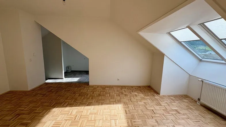Helles Wohnzimmer mit Fischgrätparkett, Dachschrägen und großen Dachfenstern, die viel Licht hereinlassen.