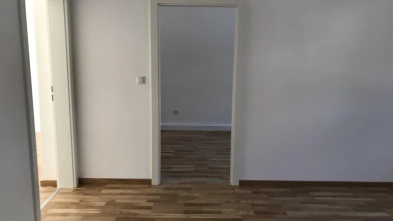 Leerer Raum mit hellem Parkettboden und zwei Türöffnungen, bereit zur individuellen Gestaltung.
