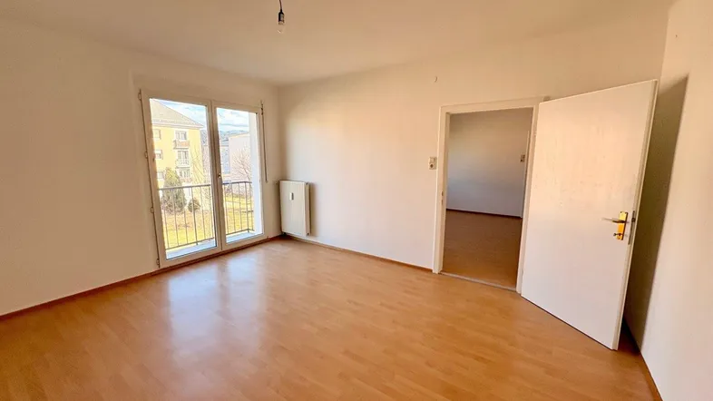 Helles Zimmer mit Laminatboden, weiß gestrichenen Wänden und Zugang zu einem kleinen Balkon.