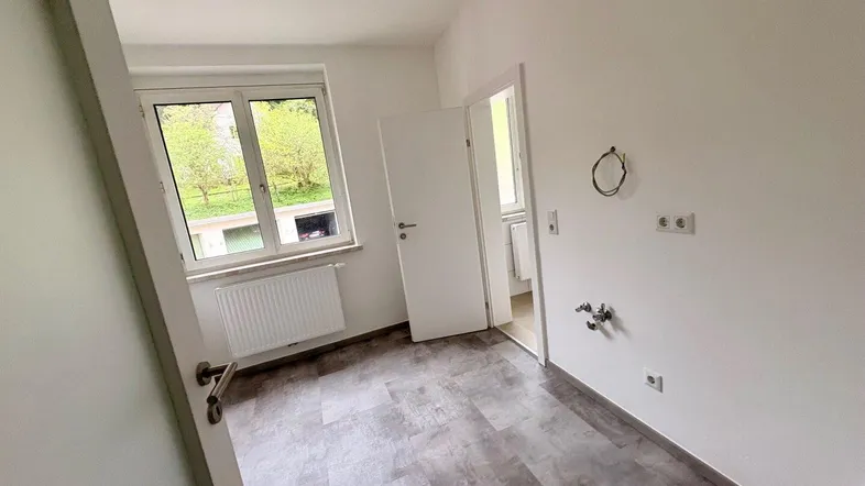 Helles Zimmer mit Fensterblick ins Grüne, Heizkörper und modernem Laminatboden.