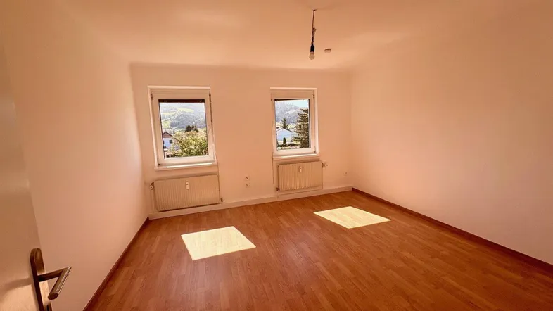 Helles Zimmer mit Parkettboden, zwei Fenstern und einem schönen Blick ins Grüne.