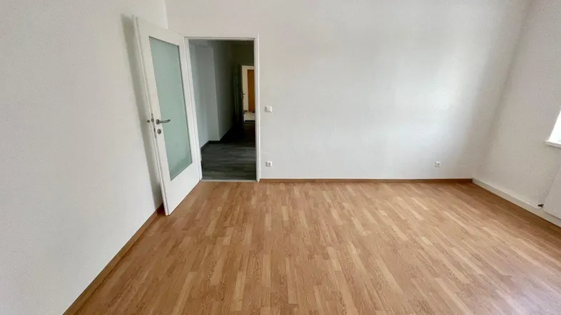 Helles Zimmer mit Laminatboden und weiß gestrichenen Wänden, bereit für die individuelle Gestaltung.