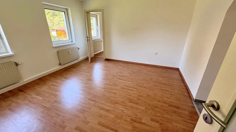 Helles Zimmer mit Laminatboden, weißen Wänden und zwei Fenstern, die viel Tageslicht hereinlassen.