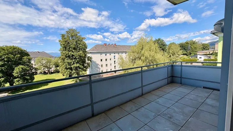Geräumiger Balkon mit Fliesenboden und Blick ins Grüne sowie auf umliegende Gebäude.