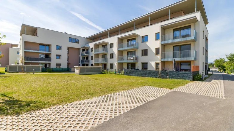 Modernes Mehrfamilienhaus mit mehreren Balkonen und gepflegter Grünfläche in sonniger Umgebung.