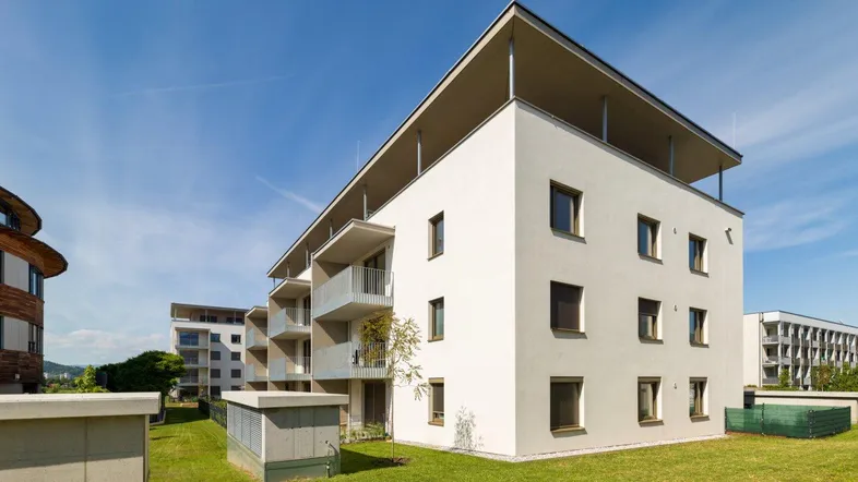 Modernes Mehrfamilienhaus mit klarer Architektur und begrünten Außenanlagen unter blauem Himmel.