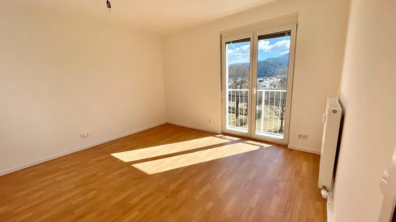 Helles Zimmer mit Holzboden, Heizkörper und Zugang zu einem französischen Balkon mit Bergblick.