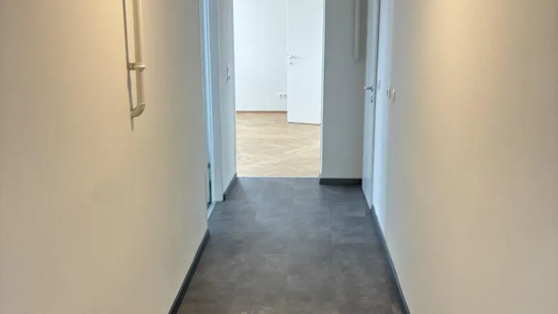 Langer, heller Flur mit dunklem Bodenbelag und weißen Wänden, der zu weiteren Räumen führt.
