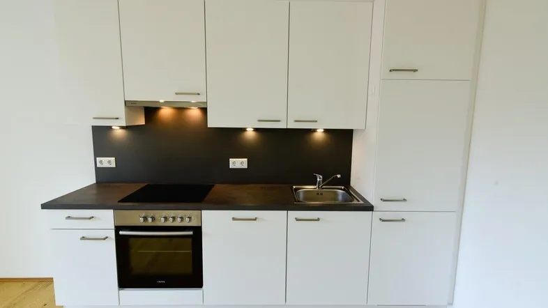 Moderne Einbauküche mit weißen Schränken, dunkler Arbeitsplatte und integrierten Geräten.