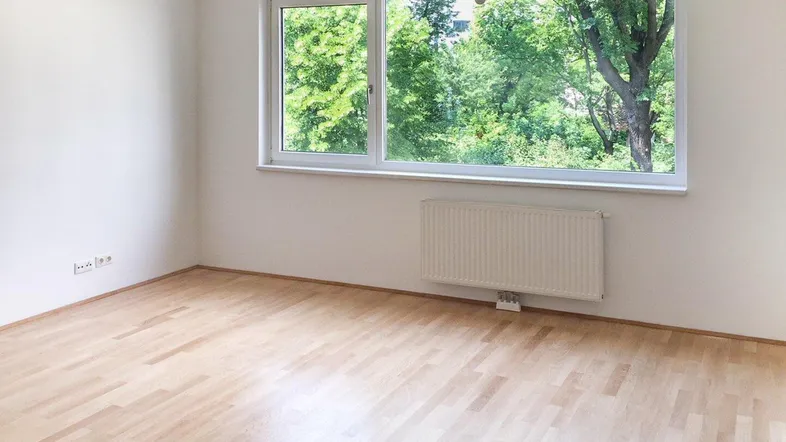 Helles Zimmer mit großen Fenstern, Blick ins Grüne und hellem Laminatboden.